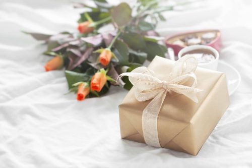 Beautiful colourful pretty gift or present in a natural paper with chocolate pralines, coffee and fresh roses on a bed. Holiday, valentine's day or surprise concept